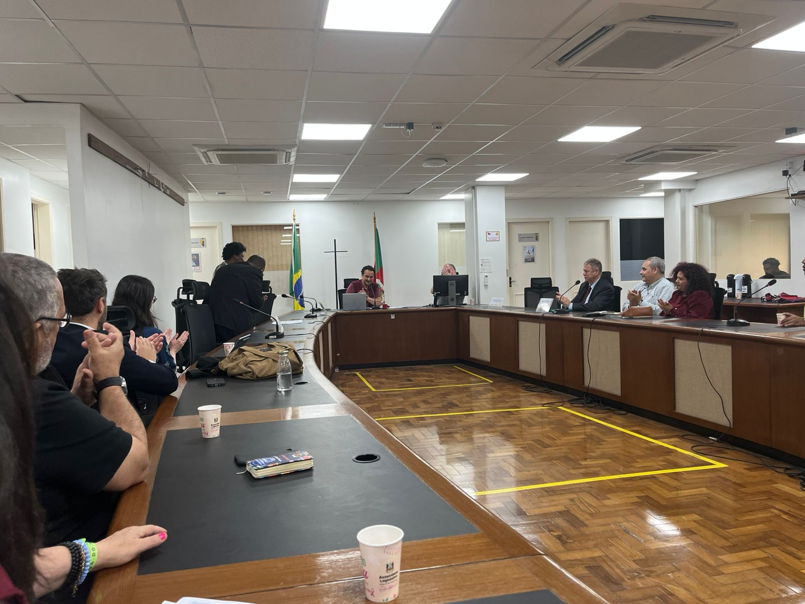 A foto mostra uma mesa de reunião com várias pessoas em volta.