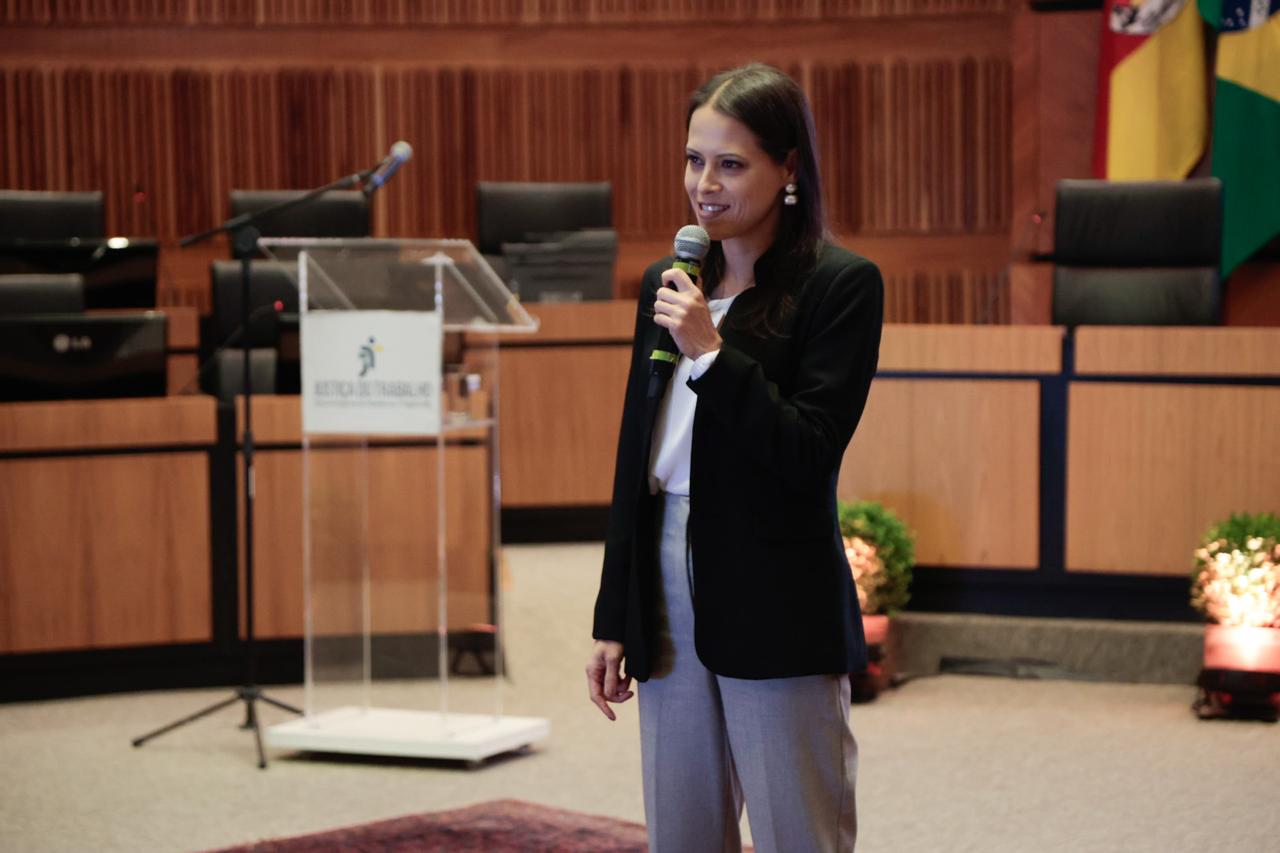 A foto mostra a servidora Natascha falando ao microfone.