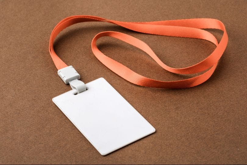 Crachá branco com corda laranja sobre fundo de cor marrom.