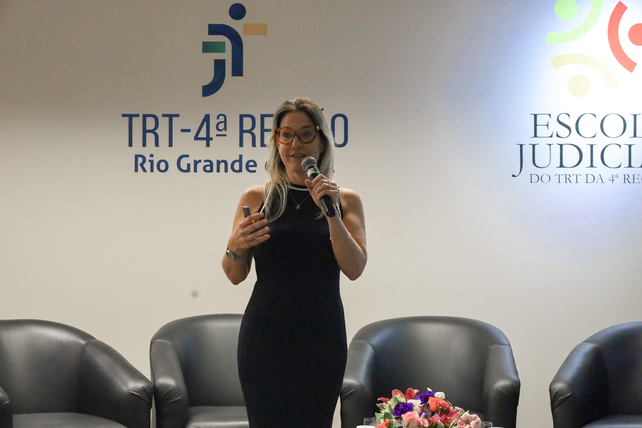 Luciana Pulvirenti, falando ao microfone, de pé, no palco.