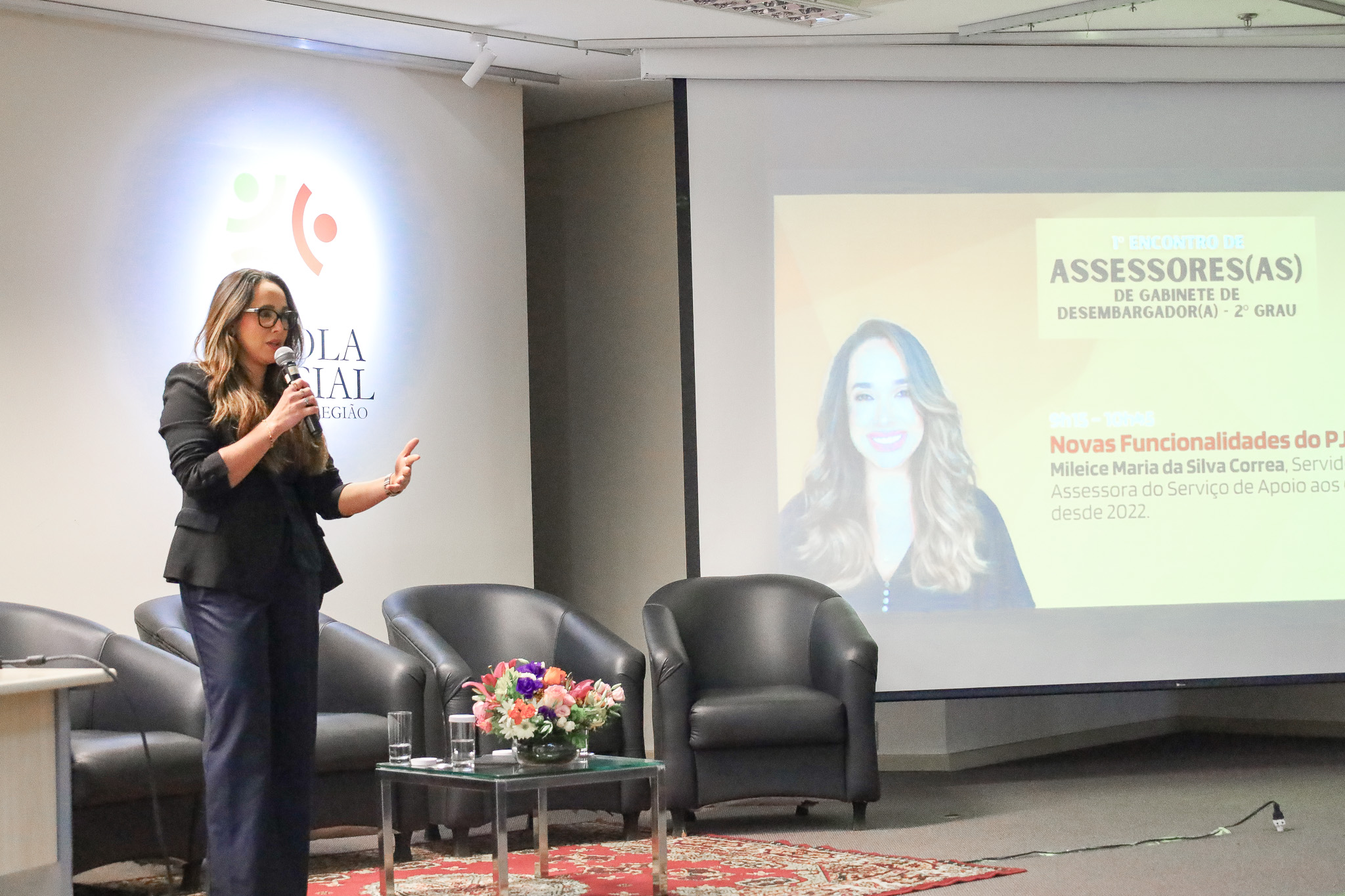 Mileice Correa, em pé, no palco. Ao lado dela, o telão com a apresentação.