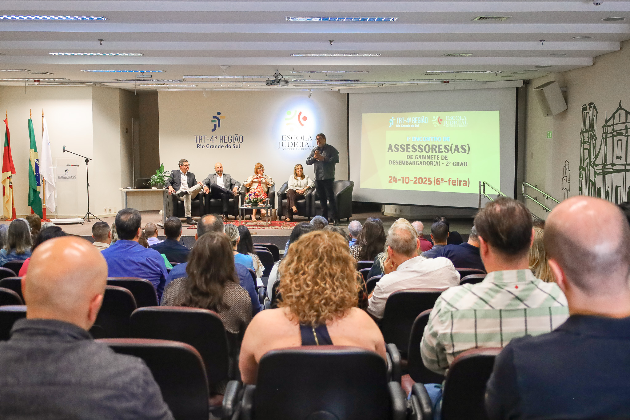 Abertura do Encontro. No palco, Aldo Jardim falando. Público aparece em primeiro plano, de costas.