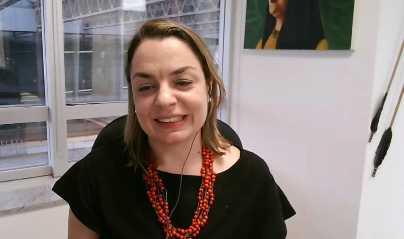 Juíza Gabriela Lacerda é uma mulher branca, de 42 anos, cabelos lisos e claros. Ela usa vestido preto e colar de contas vermelhas.