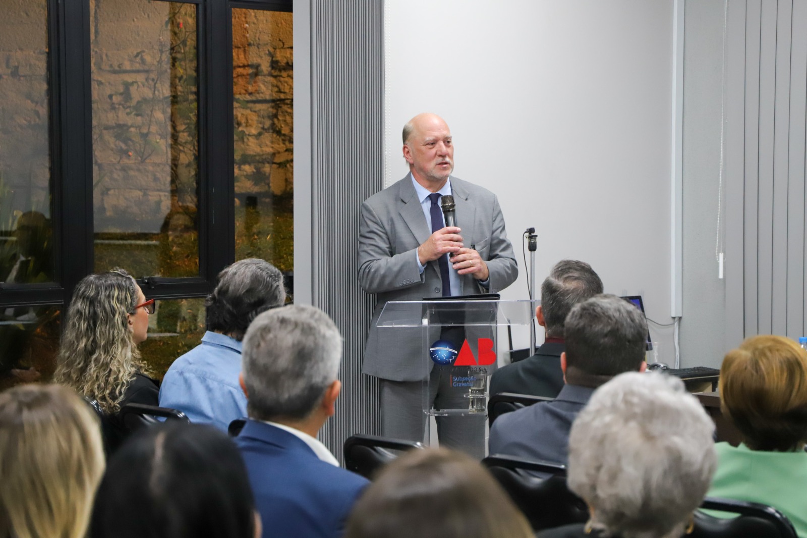 A foto mostra Martins Costa de fundo com pessoas em frente.