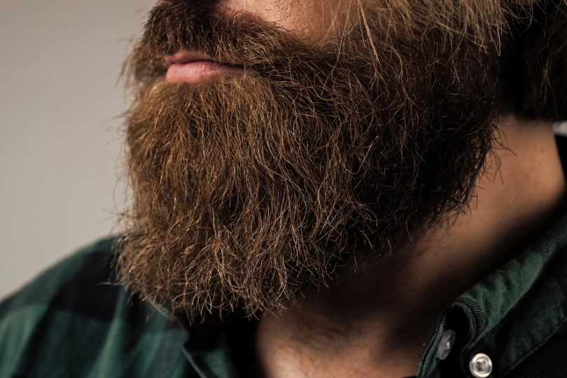 barba de cor escura. Apenas a barba e parte do pescoço são mostrados. Homem tem a pele clara e usa camisa verde.