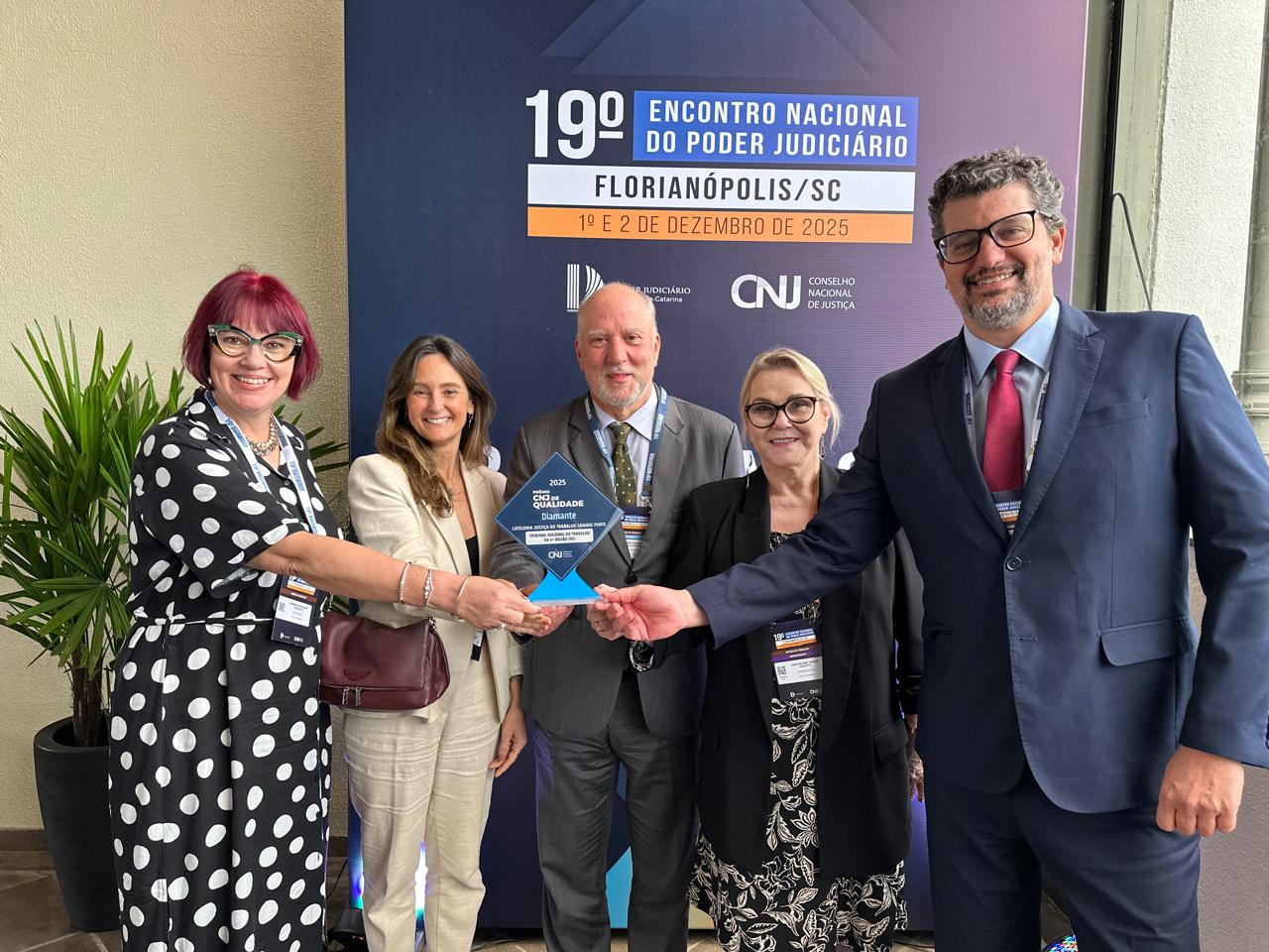 Cinco pessoas aparecem sorrindo para a foto e segurando um troféu.