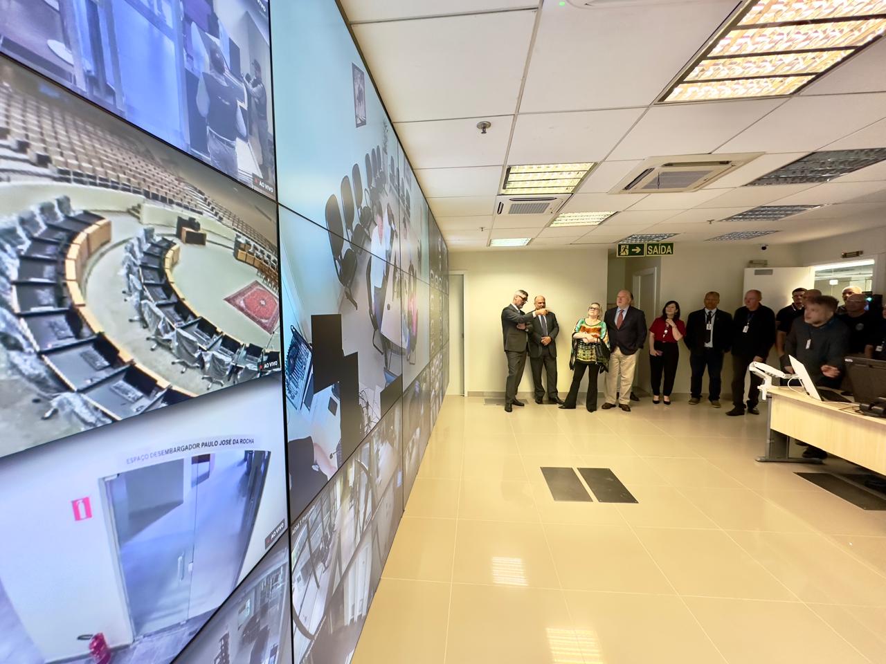 Foto da sala de segurança do TRT, aparecendo de fundo pessoas.
