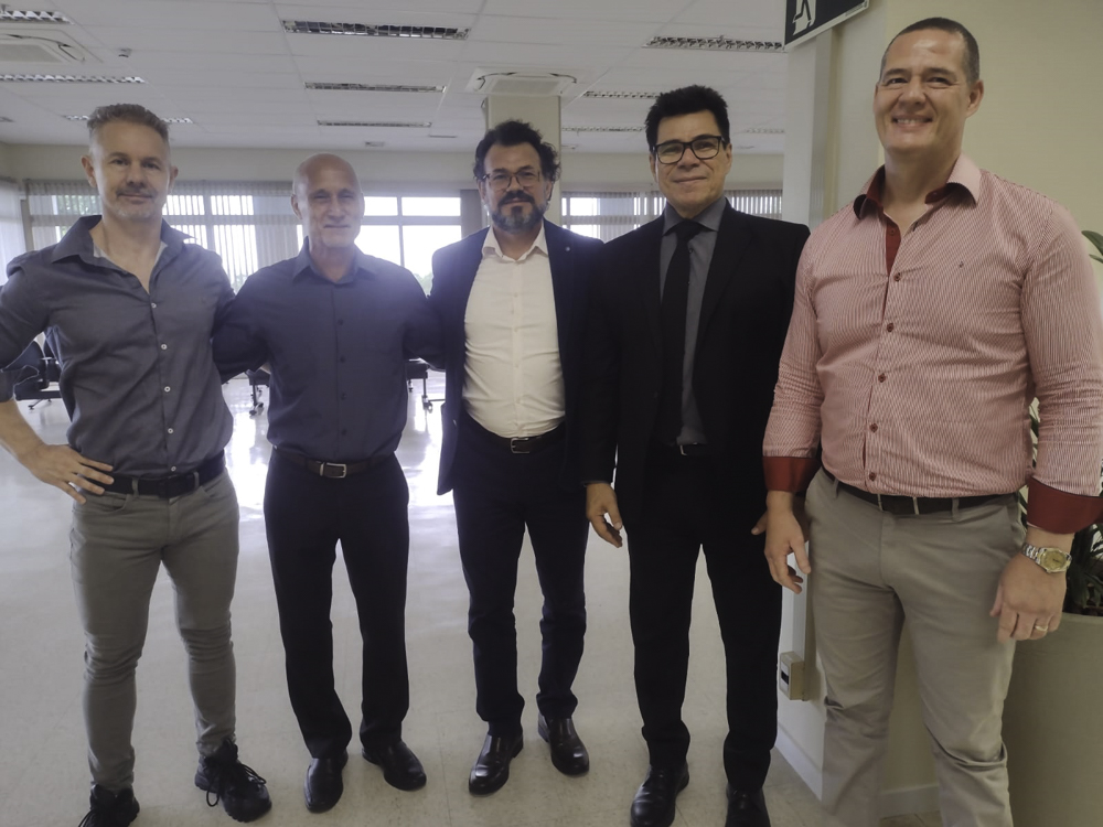 cinco pessoas aparecem sorrindo para a foto de pé. Estão no ambiente de uma secretaria de Vara do Trabalho.
