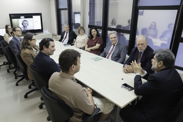 caputo bastos aparece no canto direito da foto, na ponta da mesa da conciliação. Os demais presentes estão sentados ao longo da mesa e olham para ele. O ministro fala e gesticula.