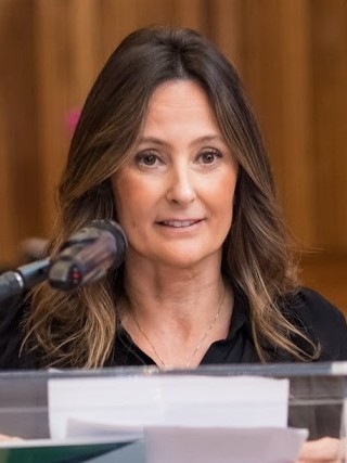 Luciana é branca, de cabelo liso e castanho. Fala ao microfone. 