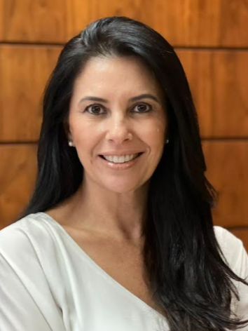 Aline é branca, de cabelo liso e preto. Sorri para a foto. 