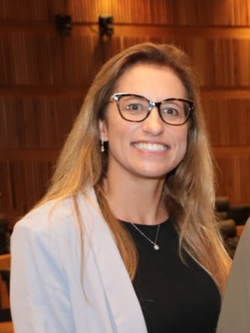 Carolina é branca e loira. Usa óculos e sorri para a foto. 