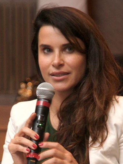 Carolina é branca e de cabelo castanho liso. Fala ao microfone. 