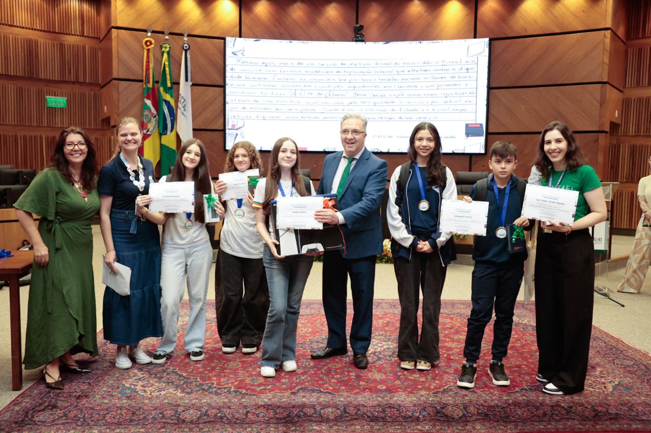 A imagem mostra uma foto posada de alunos recebendo prêmio.