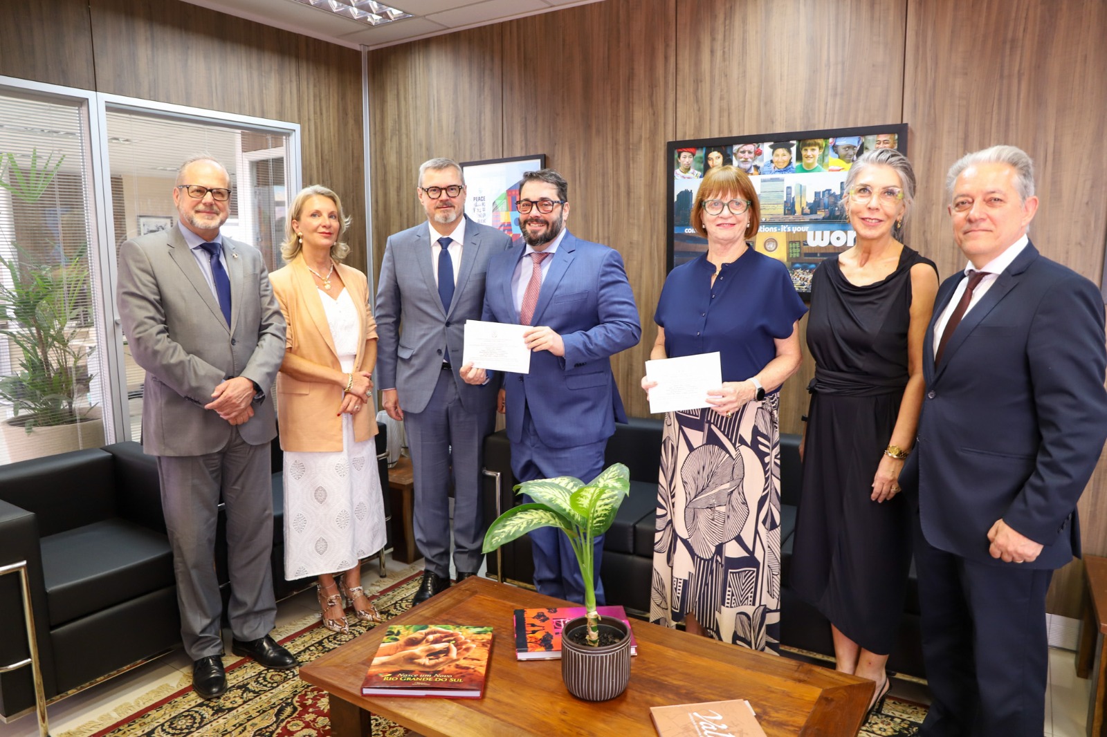 A foto mostra seis pessoas posando pra uma foto. Duas seguram o convite da posse do TJ-RS.