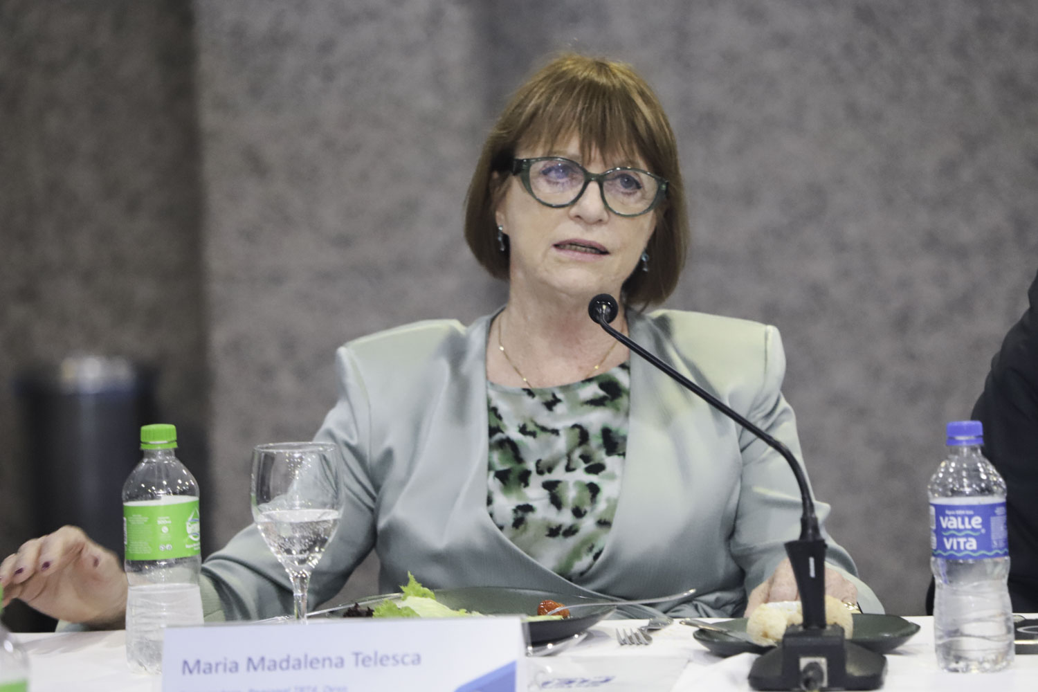 Telesca é branca e ruiva. Usa blazer e camisa verde. Fala e olha para a direita. 