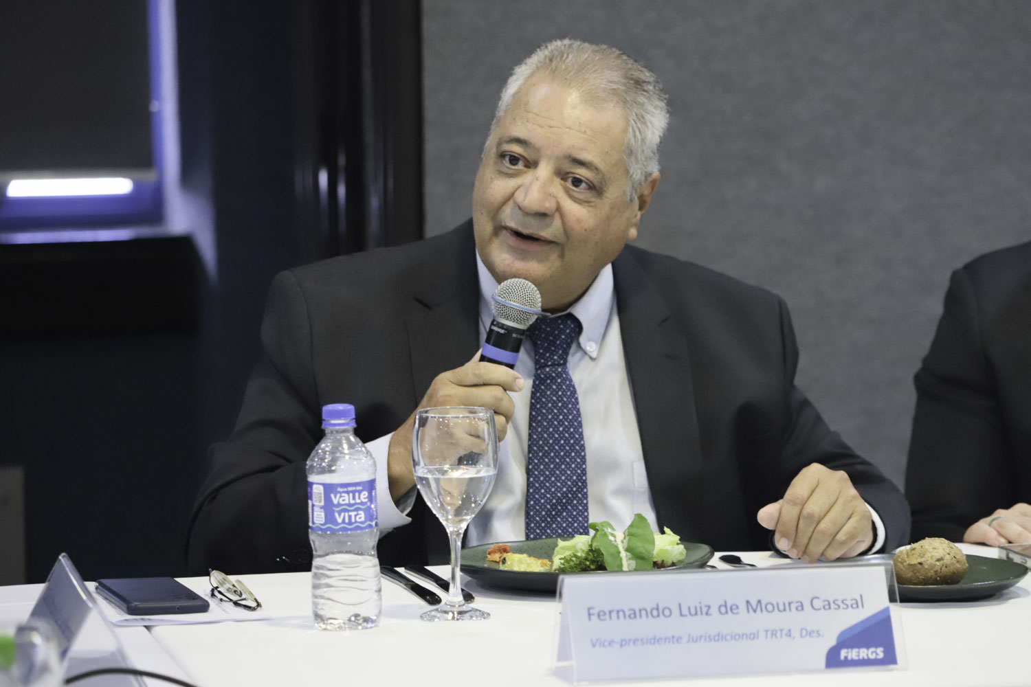 Cassal é branco e grisalho. Usa terno escuro, camisa cinza e gravata azul. Fala ao microfone olhando para a esquerda. 