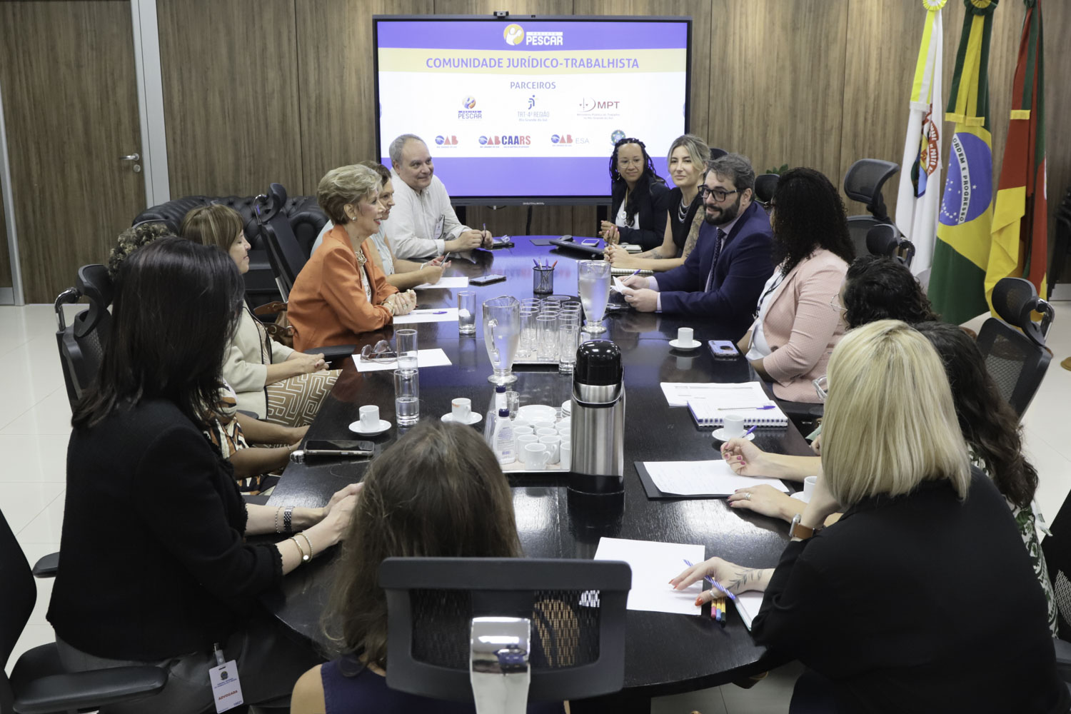 participantes da reunião em torno da mesa. presidente Alexandre está falando. ao fundo aparece uma tela ligada com o logo do Pescar