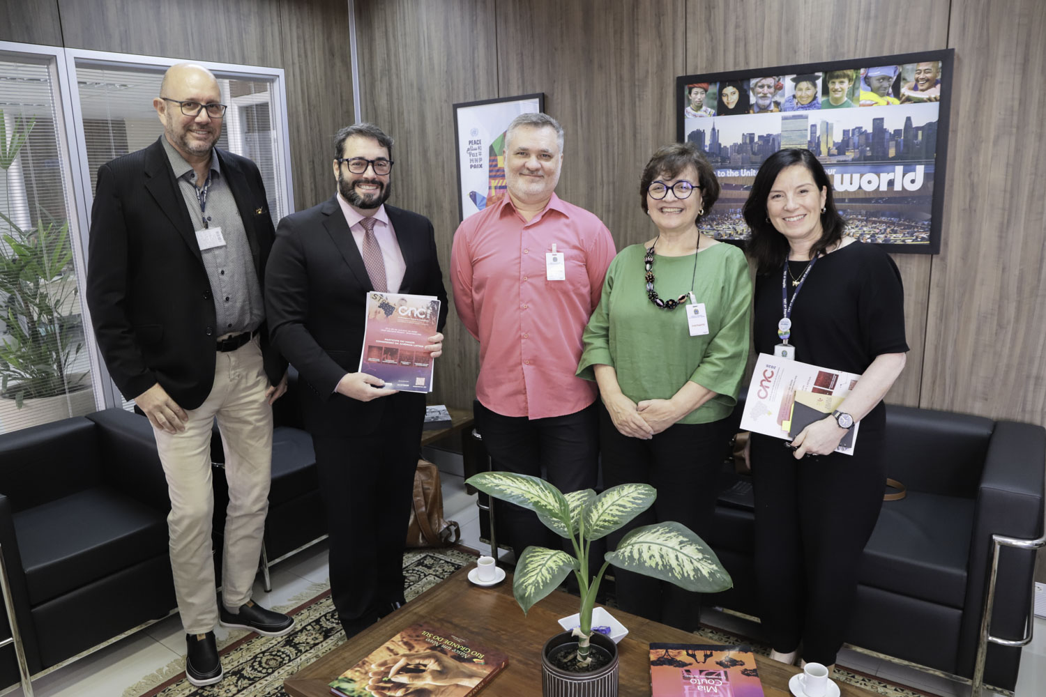 Cinco pessoas posam para a foto de pé, sorrindo. Alexandre e Enilda seguram materiais de divulgação do Congresso.