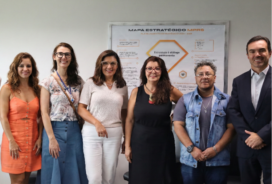 Seis integrantes do grupo posam para a fotografia alinhados à frente de um painel do Mapa Estratégico do MPRS, que traz em destaque a frase "Estratégia é diálogo permanente".