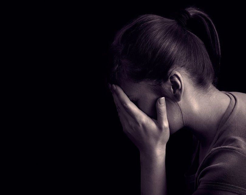 Foto ilustrativa de uma mulher sentada, com os cotovelos apoiados na mesa e as mãos sobre o rosto.