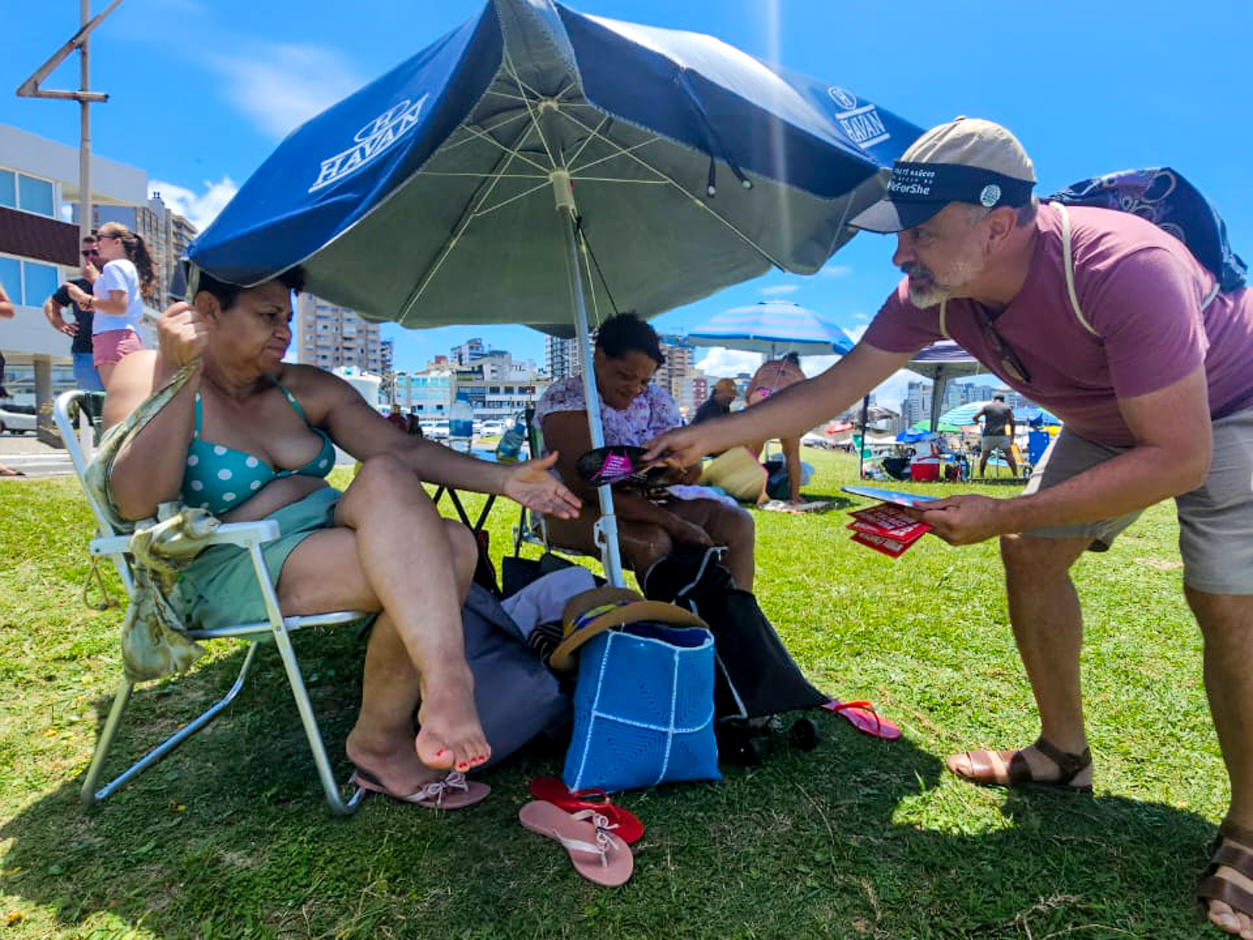 Márcio entregando material informativo a duas senhoras, na praia