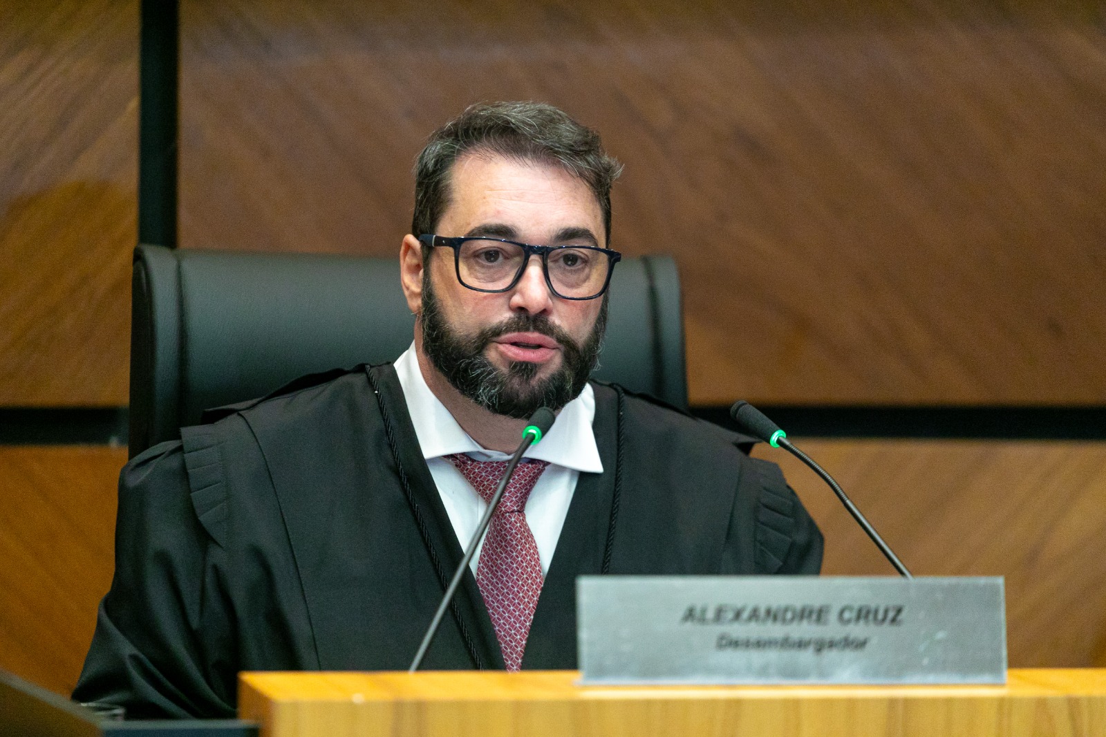 A foto mostra o desembargador Alexandre em frente a um microfone falando.