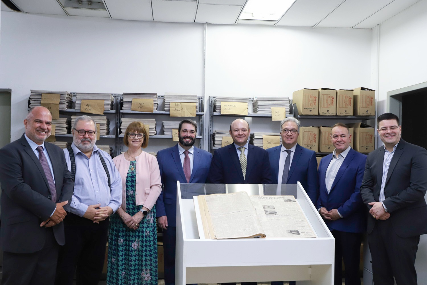 A foto mostra oito pessoas posando para foto e na frente um jornal aberto.