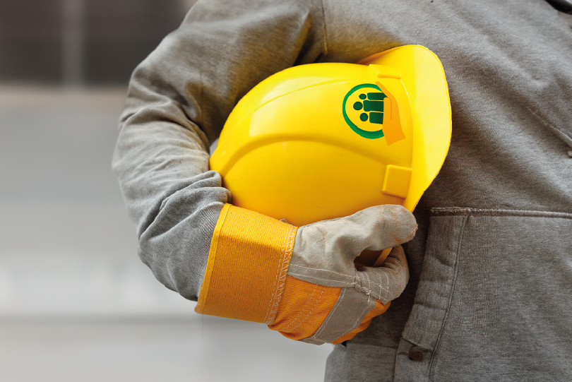 foto de um trabalhador com macacão e luvas, segurando um capacete.