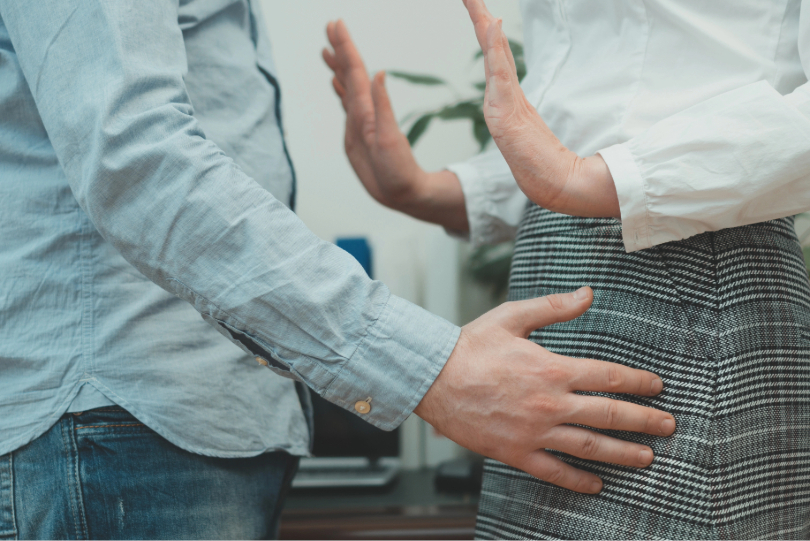 Mulher põe as mãos em frente ao corpo para afastar homem que quer tocá-la. Não há imagens do rosto deles. Ele usa camisa azul claro e calça jeans e ela camisa branca e saia em preto e branco.