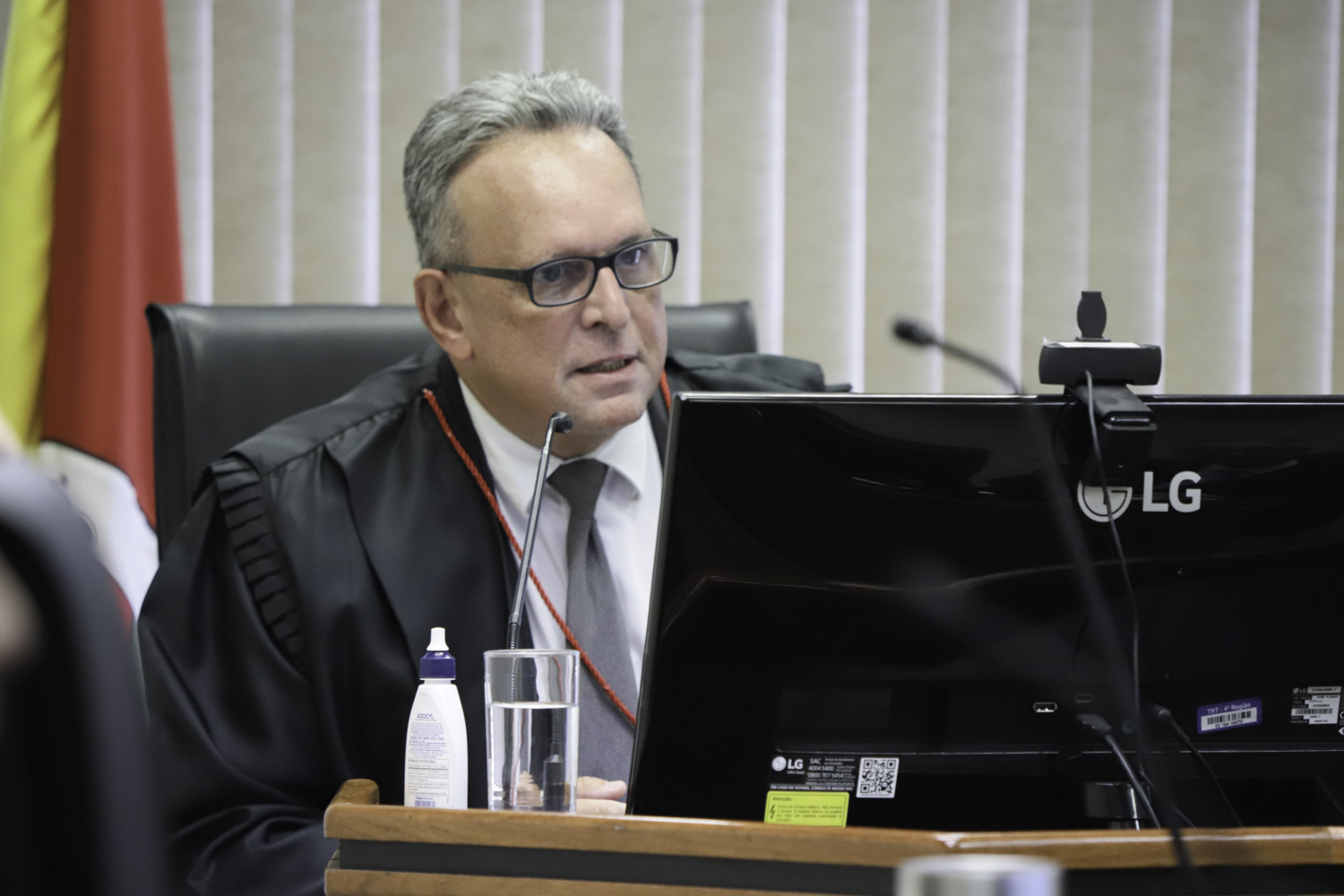 Victor é branco e grisalho. Usa óculos e veste toga. Está falando e olhando para a direita. 