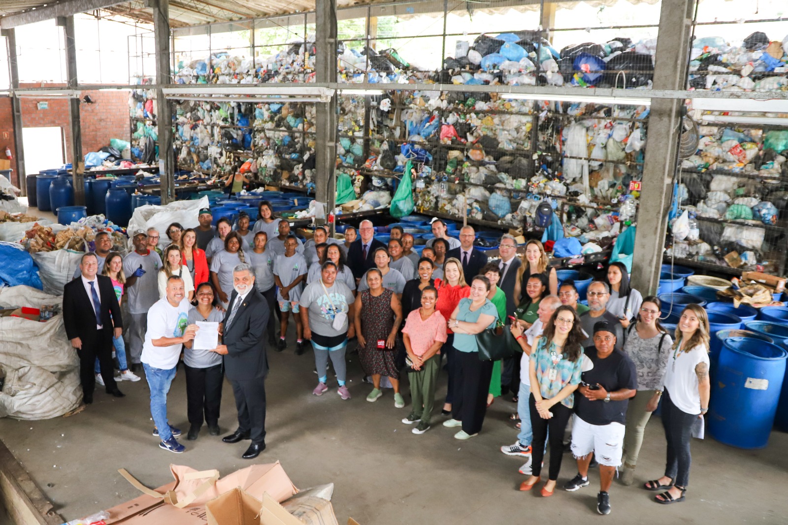 Foto feita durante a visita do presidente do TST, Lelio Bentes, ao Centro de Educação Ambiental, em 2024. Há pessoas posando para a fotografia. Ao fundo, uma grade que vai até o teto está cheia de sacos de lixo.