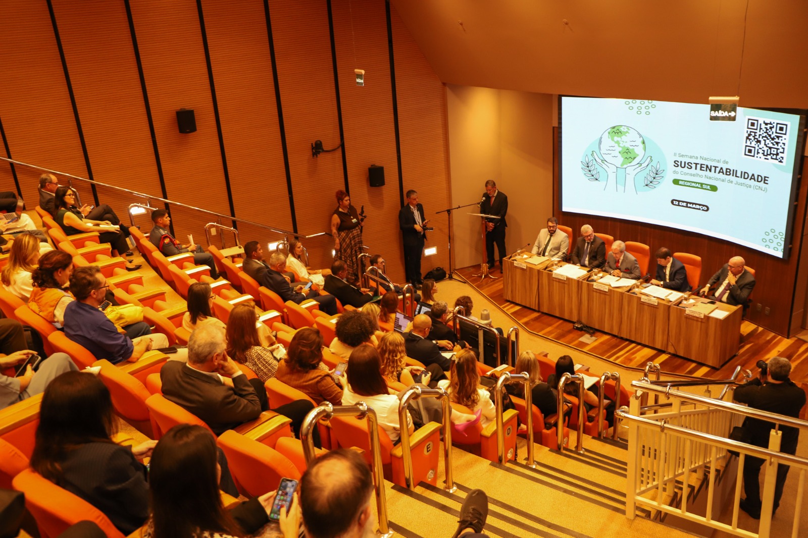 A foto mostra o evento de cima, plateia na frente e mesa de autoridades ao fundo.
