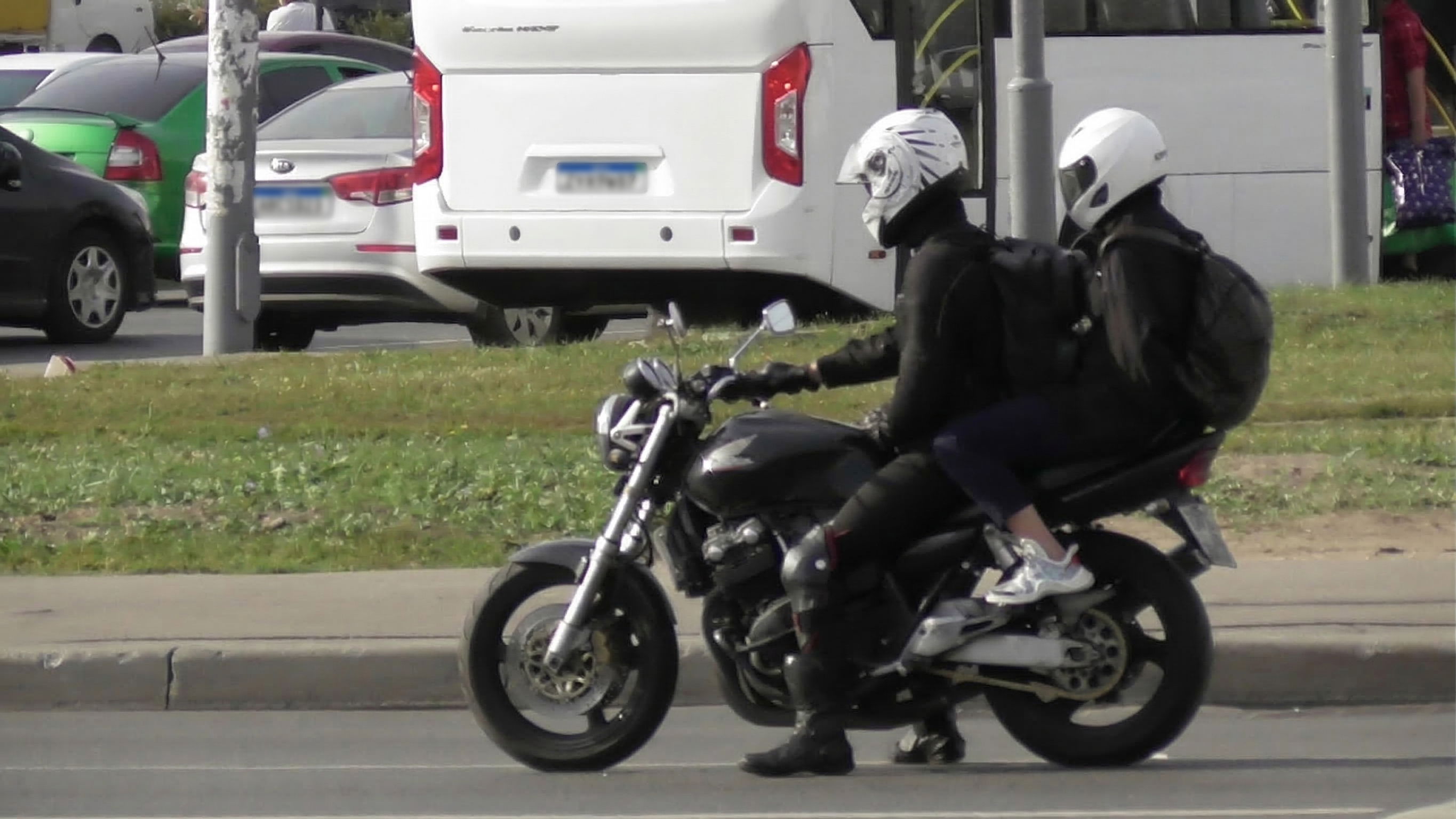 Foto ilustrativa que retrata uma motocicleta preta sendo conduzida em uma via urbana, transportando duas pessoas.