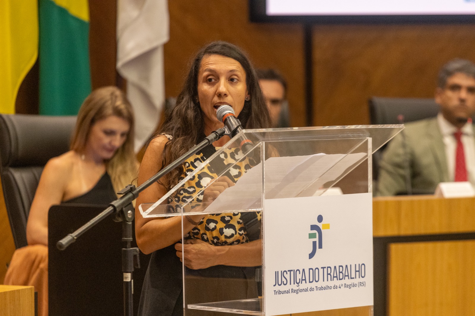 Liz é parda, tem cabelo comprido liso e escuro. fala ao microfone
