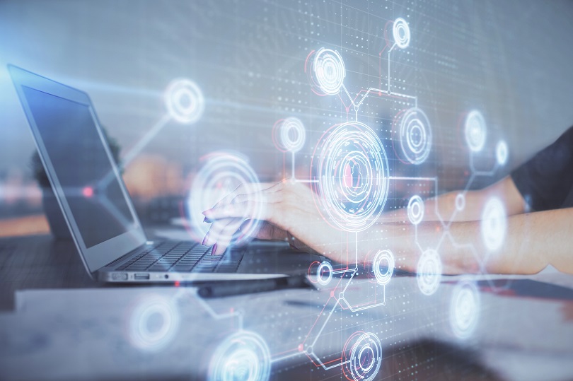 Pessoa digitando em um laptop enquanto gráficos e conexões digitais holográficas aparecem sobre a tela, representando tecnologia, dados, inovação e sistemas conectados.