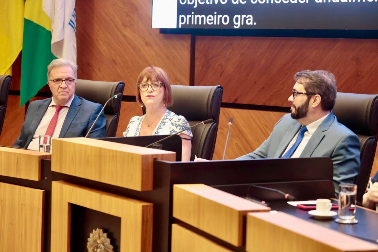 Cassou,  Maria Madalena e Alexandre na mesa oficial. Maria Madalena está ao centro, falando ao microfone.É branca, de cabelo ruivo e usa óculos de aros grandes.  