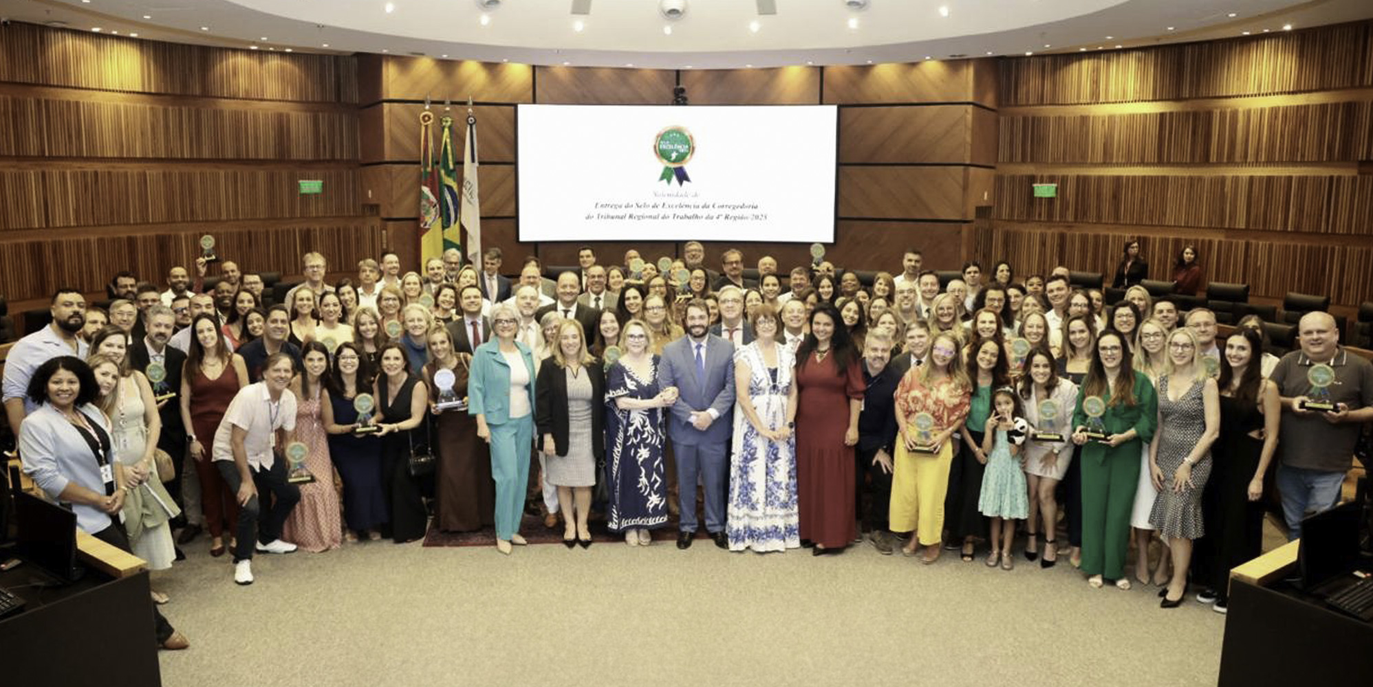 diversas pessoas posam para a foto na nave do plenário, alguns seguram o trofeu da premiação.