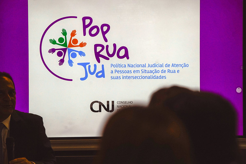 Foto de um palco. No fundo do palco, a arte da PopRuaJud.