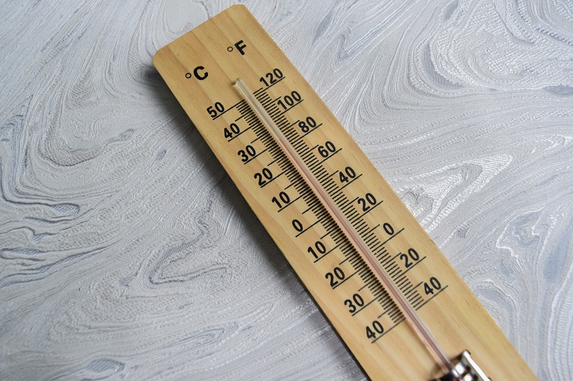 Termômetro de madeira com escalas em Celsius e Fahrenheit apoiado sobre superfície clara e texturizada.
