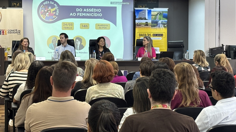 A foto mostra a desembargadora Brígida entre as autoridades numa mesa de evento.