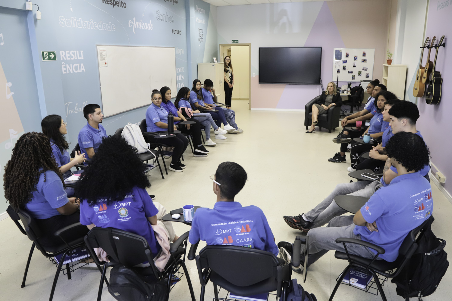 alunos sentados em círculo em primeiro plano e magistrada ao fundo. 