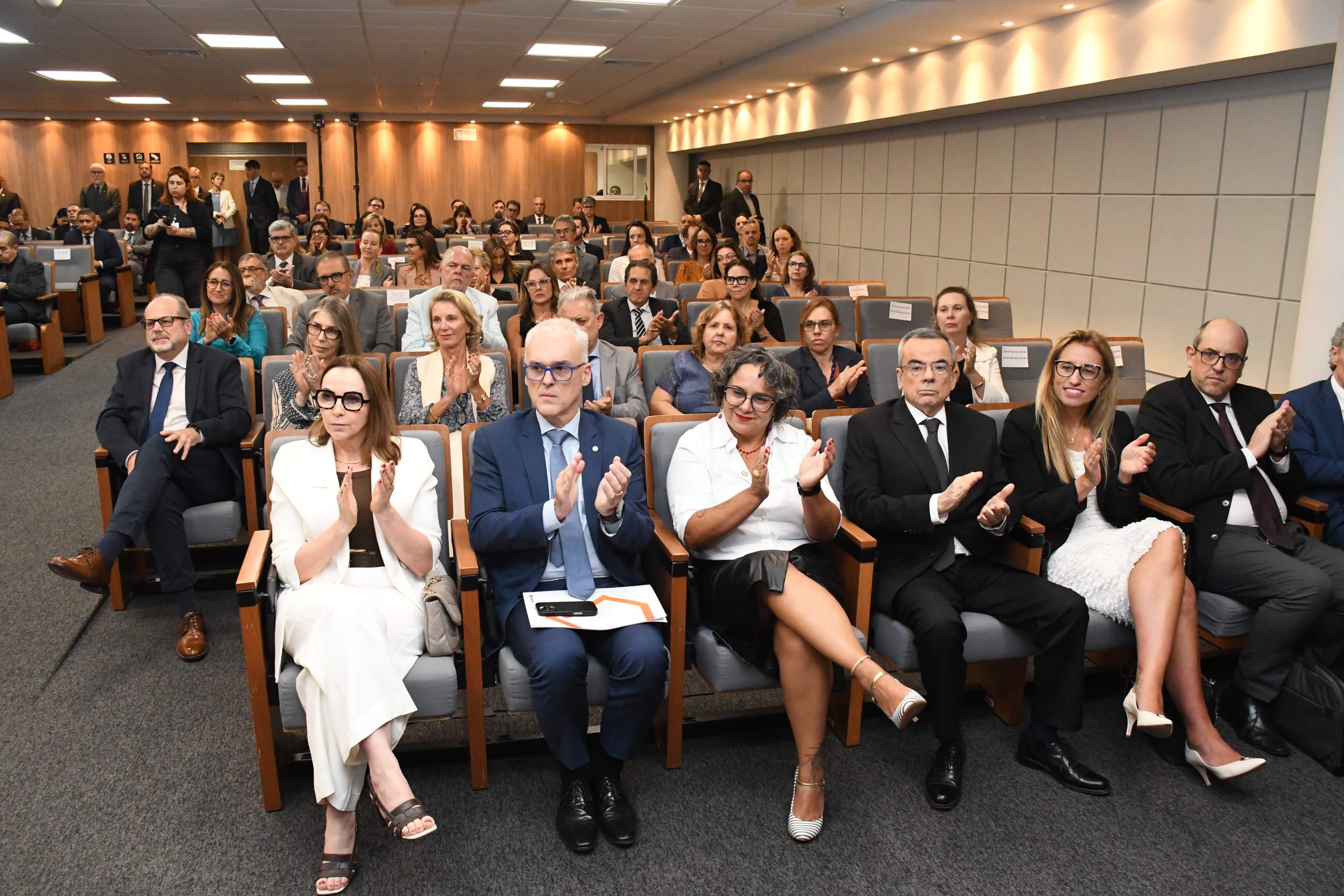 Público assistindo a cerimônia, juíza Carolina a direita, na primeira fila de cadeiras. 