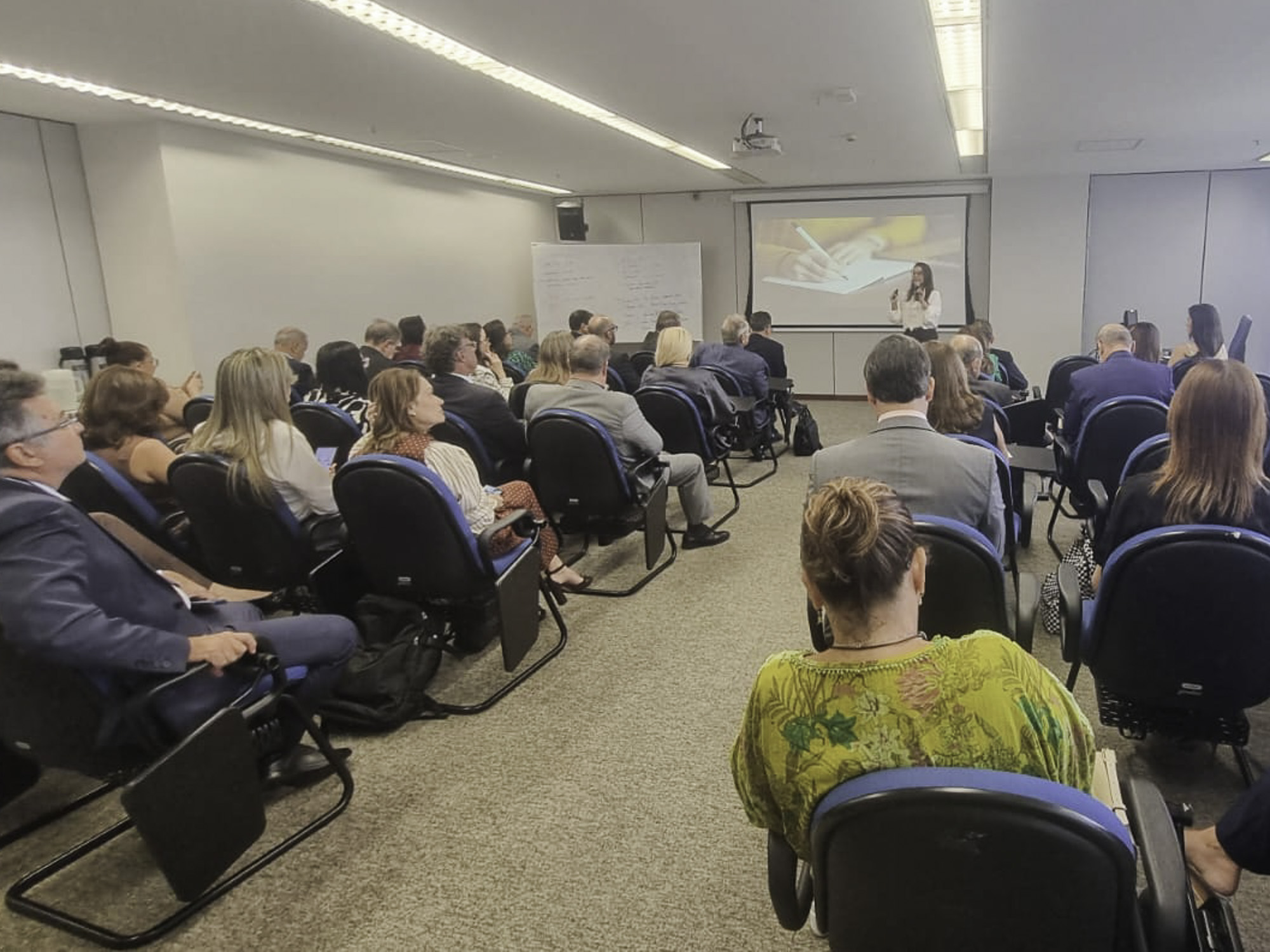 público de costas olha para a ministrante, de pé no canto direito. 
