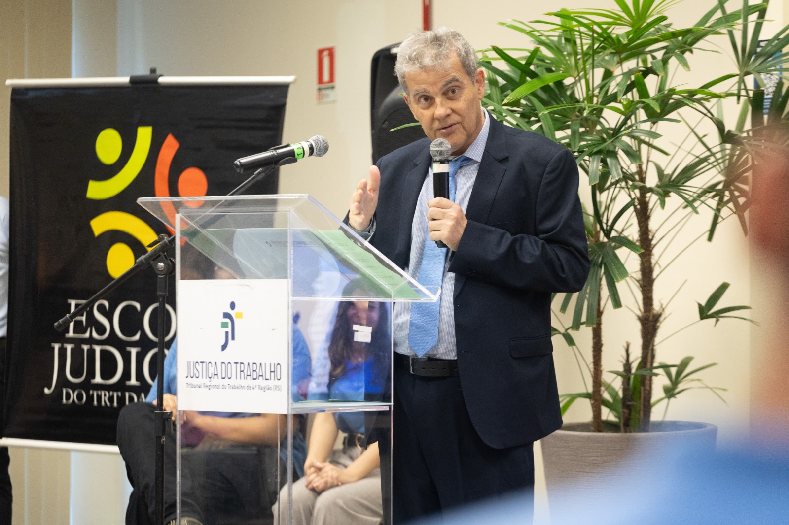 Ricardo é branco e grisalho. Está de pé e fala o microfone