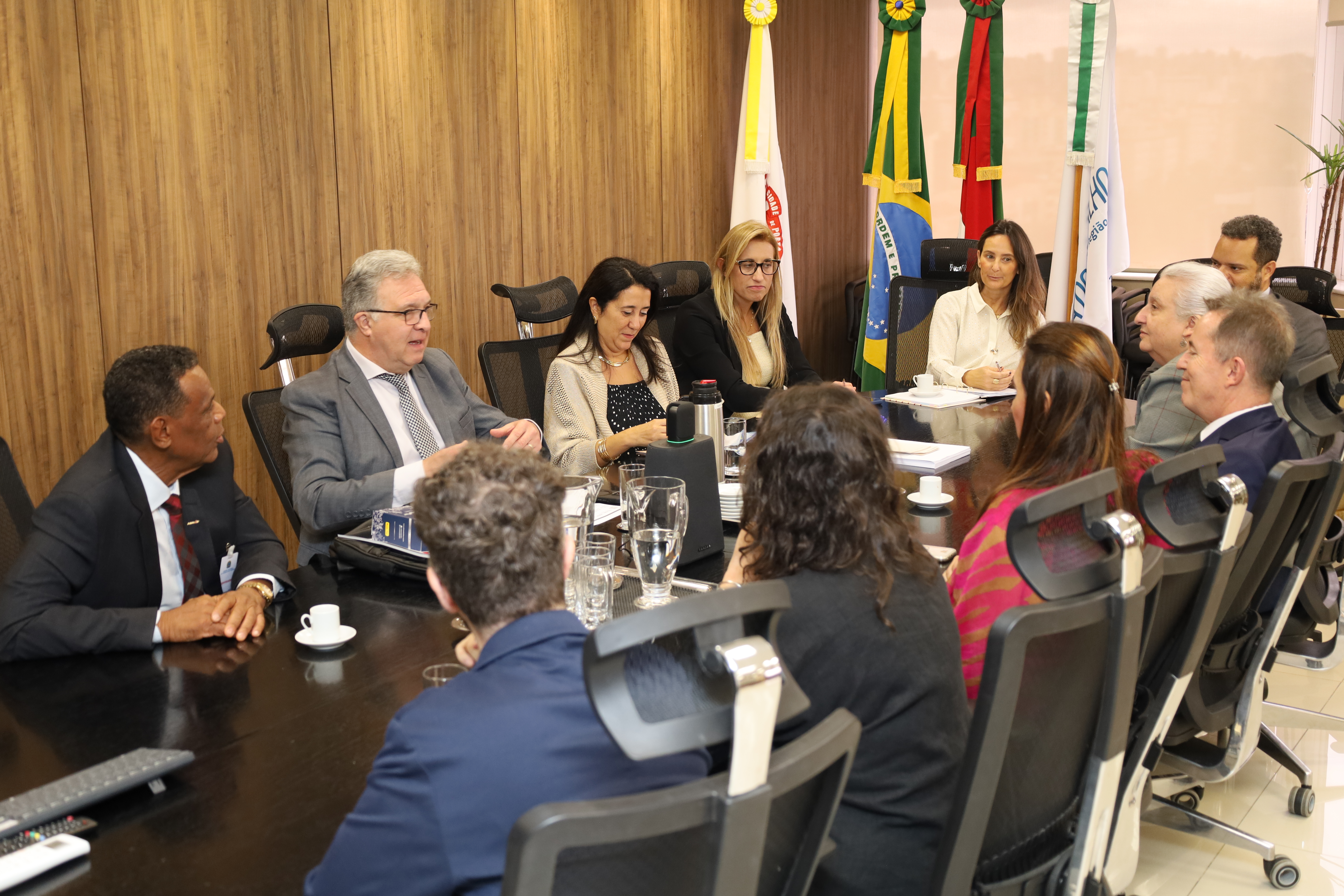 A fotografia mostra os participantes da reunião, sentados ao redor da mesa oval, conversando.