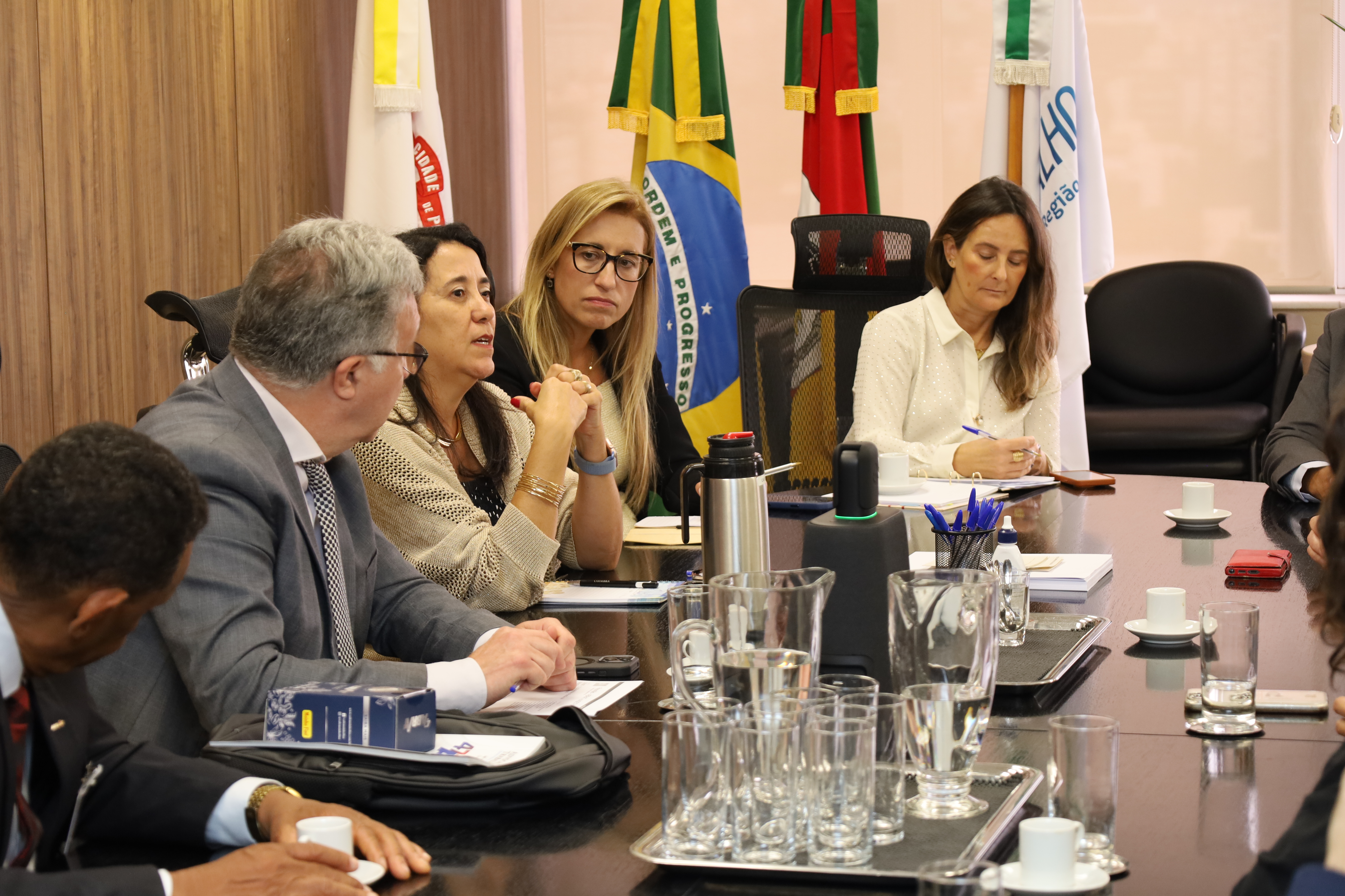 A fotografia mostra os participantes da reunião, sentados ao redor da mesa oval, conversando.