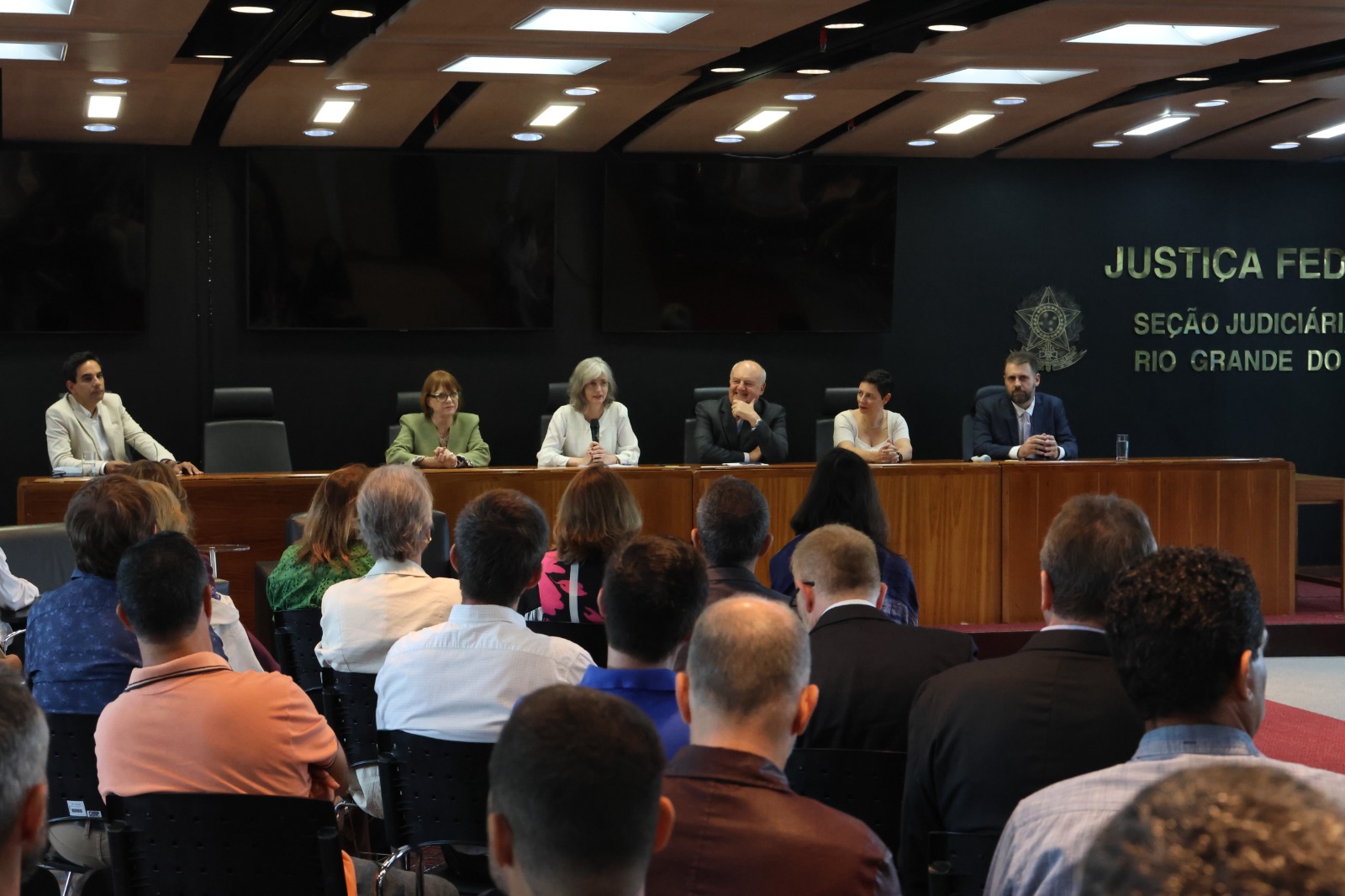 Foto do evento da Assojaf/RS, mostrando a mesa oficial da abertura  e parte do público.