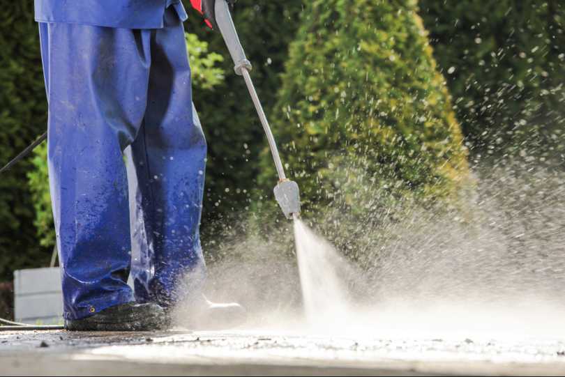 Homem de uniforme azul lava calçada. Imagem mostra apenas da cintura para baixo.