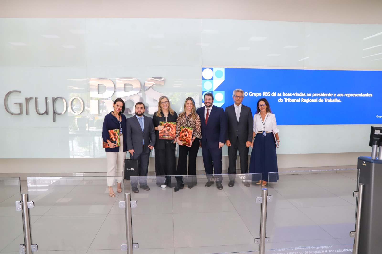Foto posada em frente a um painel com boas vindas ao TRT e o logo do grupo rbs.